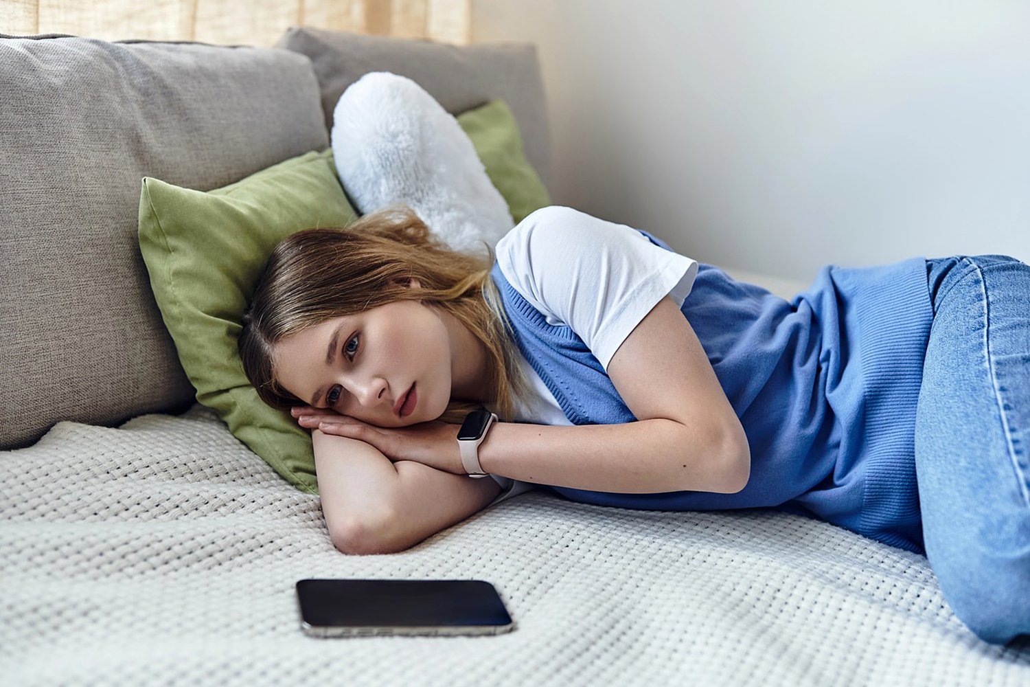 Young girl relaxes on her bed with her phone nearby, lost in thought about her day.