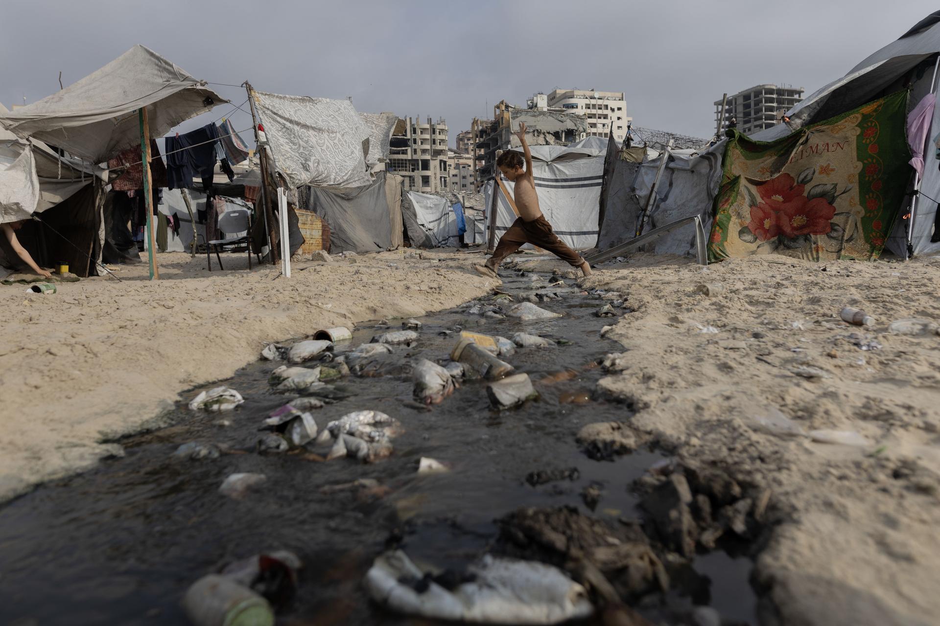 A Gazan youth crosses a stream of wastewater coming from a cluster of tents for the displaced stretching along the Mediterranean in Gaza City on Tuesday, Aug. 12, 2025. (Saher Alghorra/The New York Times)