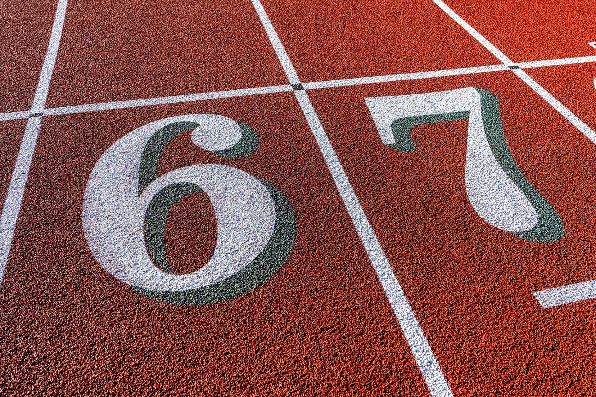 Close up photo of outdoor running track lane white numbers six seven, 6, 7, with green shadow on a new red track with white lane lines.