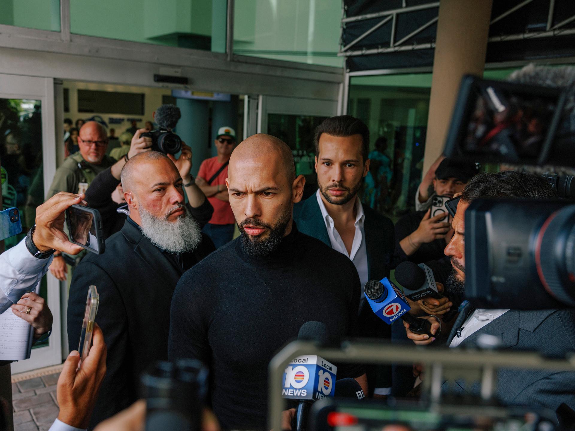 The British American online influencer Andrew Tate speaks to reporters after he and his brother Tristan Tate, obscured at center right, arrived at Fort Lauderdale-Hollywood International Airport in Florida, Feb. 27, 2025. (James Jackman/The New York Times)