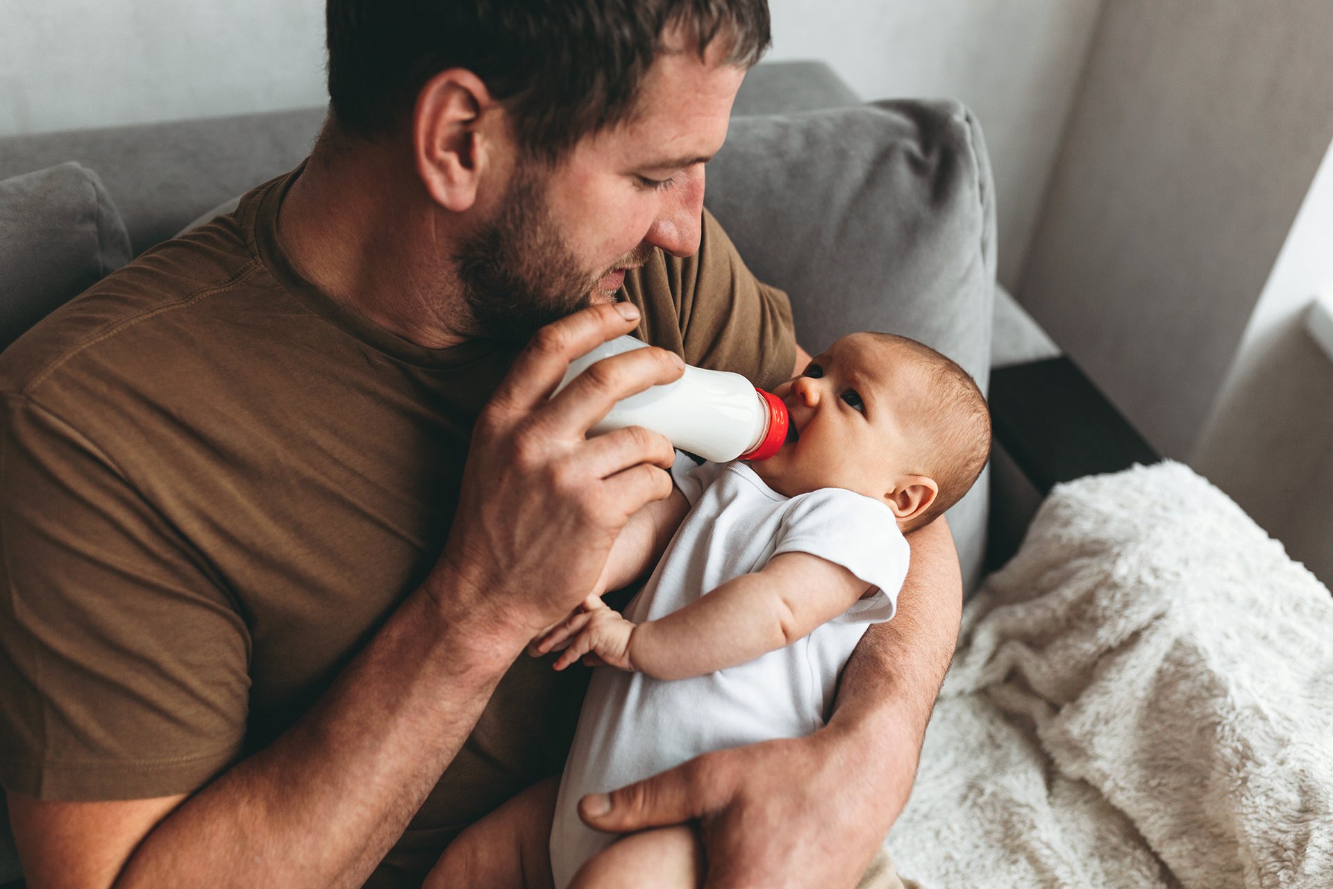 family, parenthood and people concept - father feeding little daughter with baby formula from bottle at home